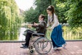 Pretty hipster young woman with dreadlock hair pushing wheelchair with elderly man, having fun in the city park in front Royalty Free Stock Photo