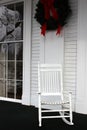 Pretty holiday scene with simple white rocking chair on porch, wreath hanging from exterior of building Royalty Free Stock Photo