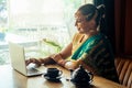 Pretty indian businesswoman in green traditional sari using laptop in office next to window. remote work and freelance