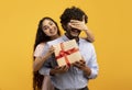 Pretty indian woman covering her boyfriend& x27;s eyes, holding gift box and greeting him with birthday or anniversary Royalty Free Stock Photo