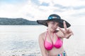 A pretty and jovial asian lady having fun at the beach. Doing a peace sign. Wearing a sun hat and a pink bikini top Royalty Free Stock Photo