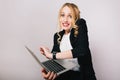 Pretty joyful blonde businesswoman with laptop talking on phone isolated on white background. Wearing office suit