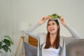 Joyful Asian female putting a plate of her green salad on her head, making a yummy face Royalty Free Stock Photo