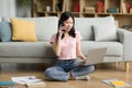 Pretty korean lady having phone conversation, sitting on floor in living room and using laptop, working from home Royalty Free Stock Photo