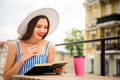 Pretty lady drinking tasty coffee to-go reading favorite novel sitting cozy in street cafe wear sun hat and striped Royalty Free Stock Photo