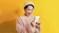 Pretty lady looks at telephone screen, chatting messages, wear warm casual hat, posing over yellow background