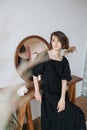 Pretty languid woman in a black dress leaning on a table with a round mirror