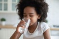 Pretty little African American girl drinking fresh water in kitchen