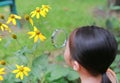 Pretty little Asian child girl with magnifying glass looks at flower in summer park Royalty Free Stock Photo