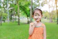 Pretty little Asian child girl with magnifying glass looks at flower in summer park Royalty Free Stock Photo