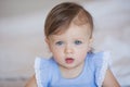 Pretty little baby girl in a blue dress sits on a bed at home Royalty Free Stock Photo