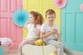 Pretty little blonde curly girl and upset boy portrait in white t-shirt on yellow, pink and blue background Royalty Free Stock Photo