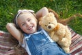 Pretty little child girl laying down with her teddy bear toy on blanket on green grass in summer smiling happily Royalty Free Stock Photo