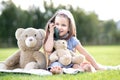 Pretty little child girl sitting in summer park together with her teddy bear toy talking on mobile phone smiling happily outdoors Royalty Free Stock Photo