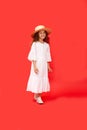 Cute little curly girl fashion pretty model with curly hair in straw hat and long white dress, isolated red background. Royalty Free Stock Photo