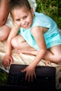 A pretty little funny girl with a laptop on the grass in nature Royalty Free Stock Photo