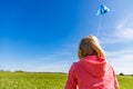 Pretty little girl with blond hair on field in pink sweatshirt looks at blue dragon in blue sky with soft clouds Royalty Free Stock Photo