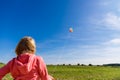 Pretty little girl with blond hair in a field in a pink sweatshirt looks at a colorful kite in a blue sky with soft clouds