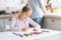 Pretty little girl busy with drawing at kitchen table