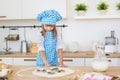 Pretty little girl in a cook clothes pushes by a cake tin on a dough on a table