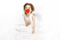 A cute little girl in dress and white wings, sitting on a fur, holding a red heart on her lips, over white background. Royalty Free Stock Photo