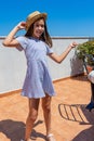 Pretty little girl dressed in a white and blue striped dress and a straw hat posing fun on the terrace of her house Royalty Free Stock Photo