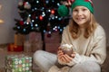 Pretty little girl with funny hat near christmas tree with new years gifts and hot chocolate with marshmallows