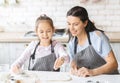 Pretty little girl and her attractive mom preparing pastry together