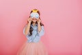 Pretty little girl with long brunette hair in tulle skirt holding sleep mask with blue eyes and golden crown  on Royalty Free Stock Photo