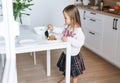 Pretty little girl with long hair puts on vegetable salad in kitchen with bright interior at home