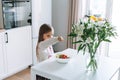 Pretty little girl with long hair sprinkles salt on vegetable salad in kitchen with bright interior at home