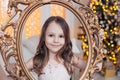 Pretty little girl posing with golden vintage frame against Christmas tree indoors. Royalty Free Stock Photo