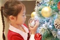 Pretty little girl in red dress holding decorative ball of christmas tree in the winter season and happy new year Royalty Free Stock Photo