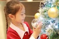 Pretty little girl in red dress holding decorative ball of christmas tree in the winter season and happy new year Royalty Free Stock Photo