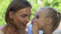Pretty little girl sharing secret with smiling mom, trustful relations in family