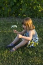 Pretty little girl sitting in lawn holding a small bouquet of wildflowers