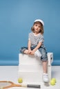 pretty little girl sitting on white boxes with tennis raquet and balls