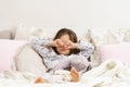 Pretty little girl in sleepwear lying on bed and rub eyes with fists. Portrait of awaking child. Kid wake up at morning.