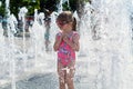 A pretty little girl standing under the jets of an open fountain on a hot day.