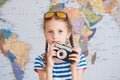 Pretty little girl in striped sailor shirt and sunglasses with vintage camere in hands on world map background Royalty Free Stock Photo