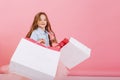 Pretty little girl walking with big white packages on pink background, smiling to side. Cute friendly child