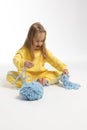 Pretty little girl in yellow clothes plays with ball of blue thread. Child model with long blond hair sits in studio on Royalty Free Stock Photo