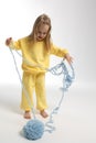 Pretty little girl in yellow clothes plays with ball of blue thread. Child model with long blond hair sits in studio on Royalty Free Stock Photo