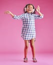 A pretty little mixed race girl with curly hair listening to music while wearing headphones against a pink copyspace Royalty Free Stock Photo