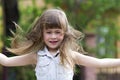 Pretty little preschool girl in sleeveless white dress with beautiful long blond hair blown by wind, funny toothless smile and spr Royalty Free Stock Photo