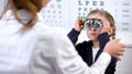 Pretty little schoolgirl visiting oculist for measuring eyesight with phoropter