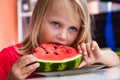 Pretty little toddler girl 4 year eating watermelon close-up at home. Funny blond child portrait with watermelon indoors, looking Royalty Free Stock Photo