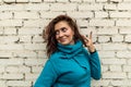 A pretty long-haired young woman wearing a blue knitted dress is standing against a white brick wall Royalty Free Stock Photo