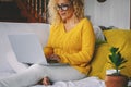 Pretty middle age woman writing on laptop and smiling. Single lady using computer alone at home. Blonde female adult enjoy leisure Royalty Free Stock Photo