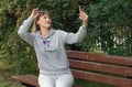 Middle aged woman, european, blonde, 45 years old, sitting on a park bench and taking a selfie Royalty Free Stock Photo